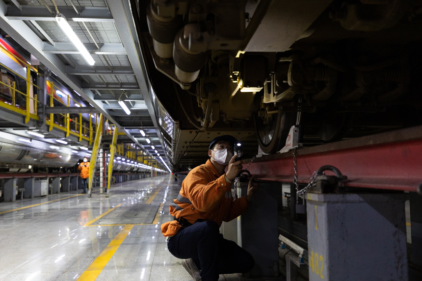 一名動車組機械師半蹲著，拿著手電筒仰望著對動車組進行檢查。李桐 攝
