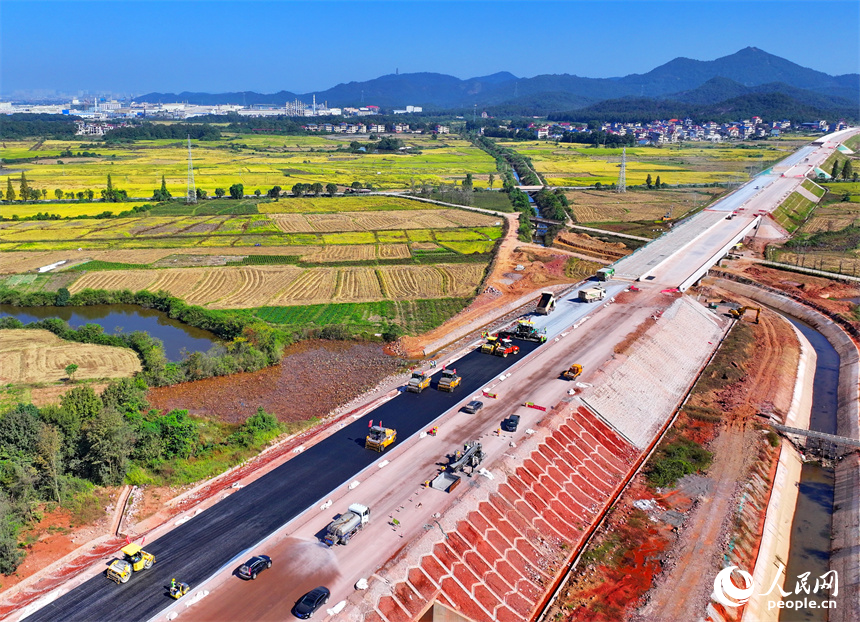 工人在加緊鋪設瀝青路面，一片繁忙施工景象。人民網 朱海鵬攝