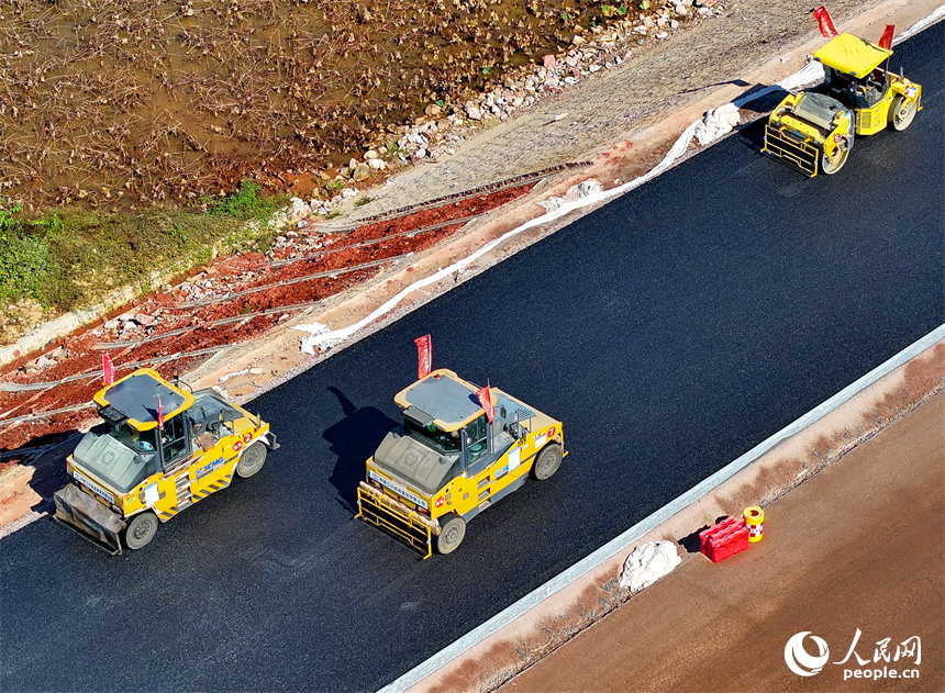 工人在加緊鋪設瀝青路面，一片繁忙施工景象。人民網 朱海鵬攝