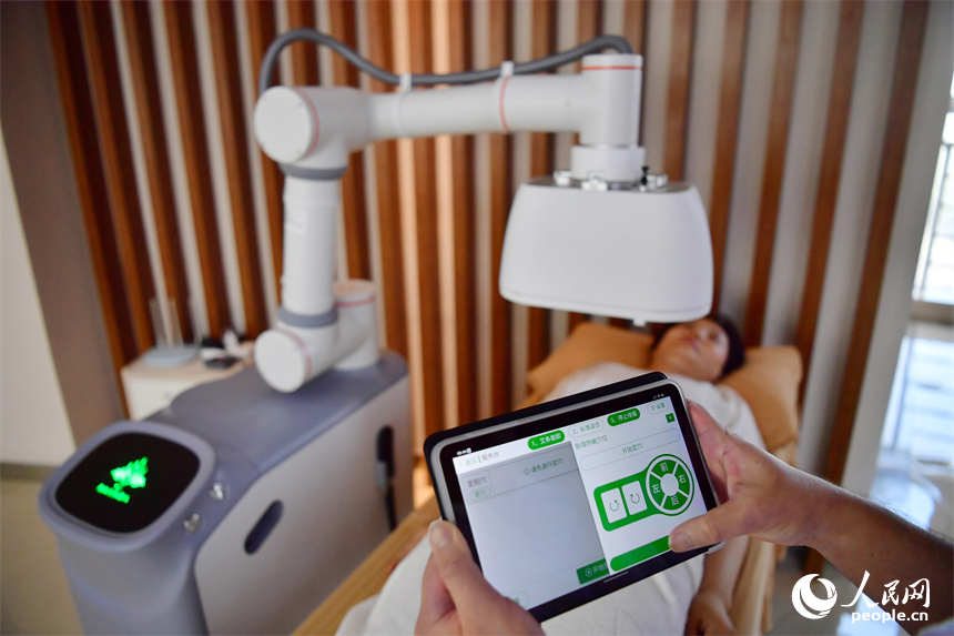 江西中醫藥大學附屬醫院的醫生正通過平板電腦上的App操作熱敏灸機器人，對病人進行熱敏灸的治療。人民網記者 時雨攝