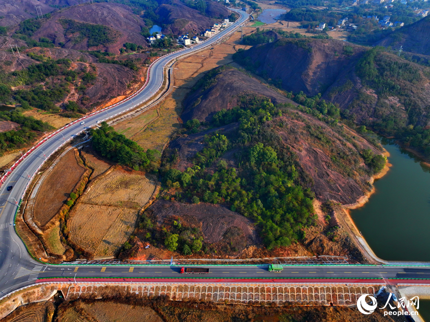 上饒市弋陽縣圭峰鎮，車輛在蜿蜒的公路上穿行，與沿線丹霞地貌山丘相映成景。人民網 朱海鵬攝