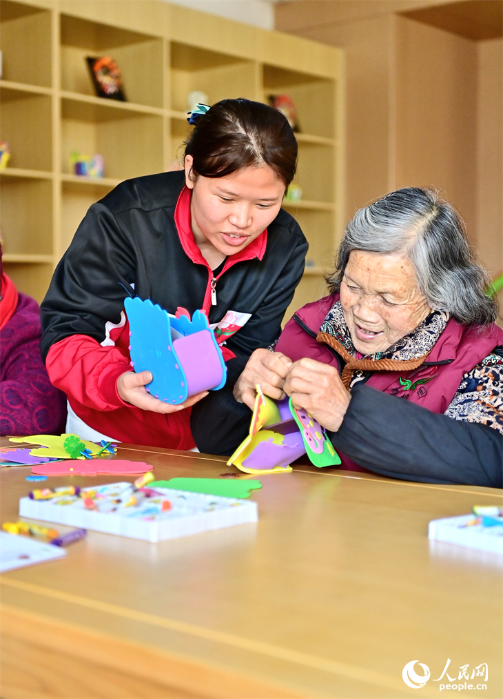 贛州市南康區蟠桃園老年公寓，護工在陪伴老人制作手工擺件。人民網 朱海鵬攝