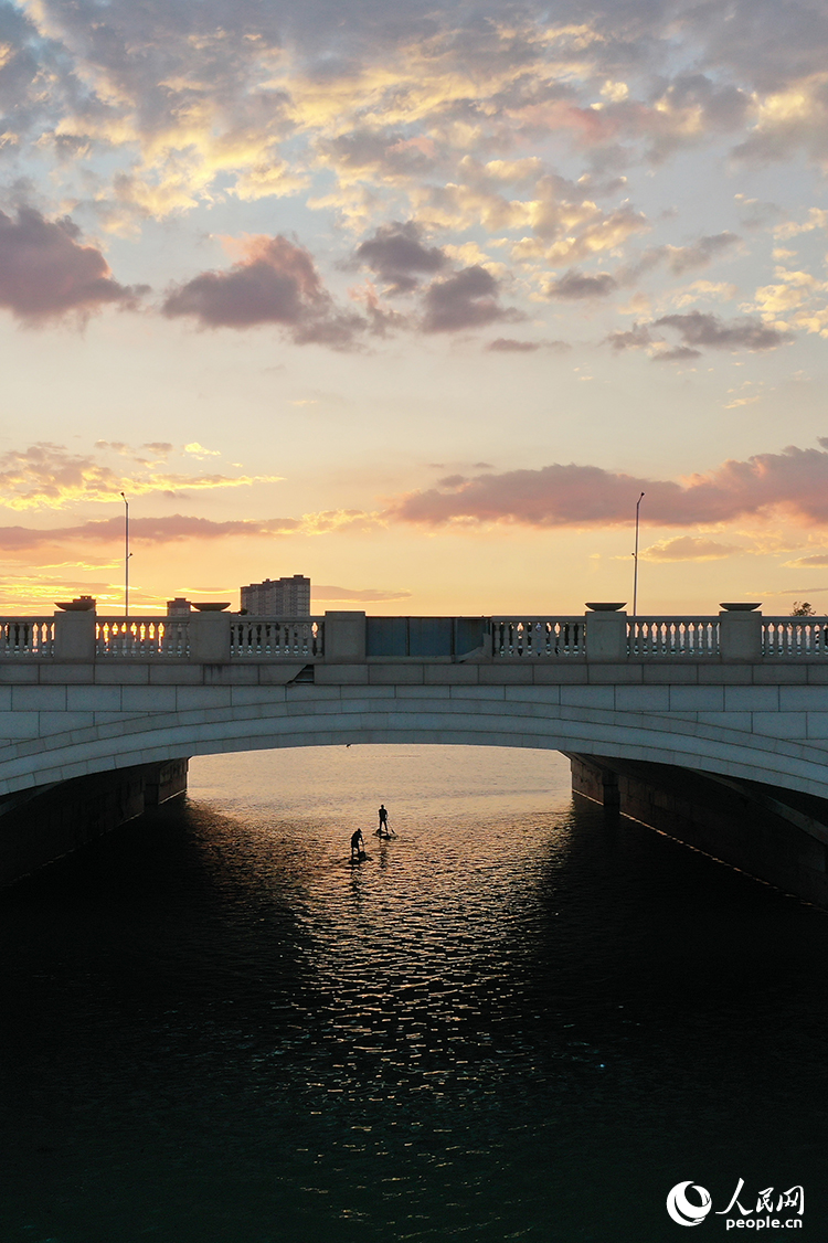 夕陽下，紅谷灘區九龍湖泛著金色波光，槳板愛好者們正在揮槳劃行穿越橋洞。人民網記者 時雨攝