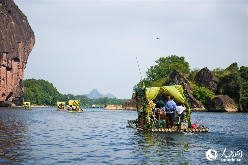 丹霞巖壁與碧水相映，游客坐在竹筏上欣賞山水奇峰。人民網 涂詩軒攝